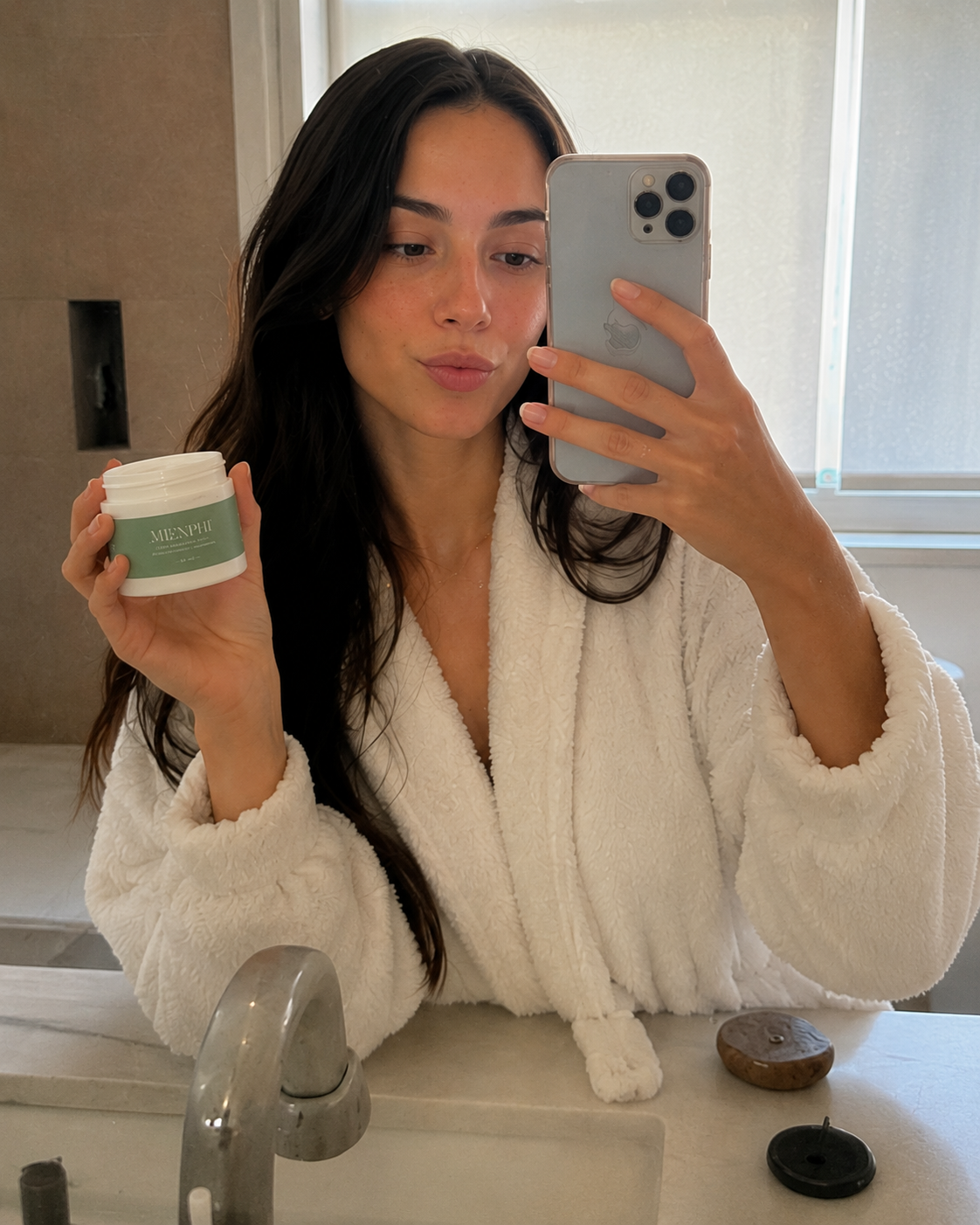 Woman in a white robe taking a bathroom mirror selfie with Menphi